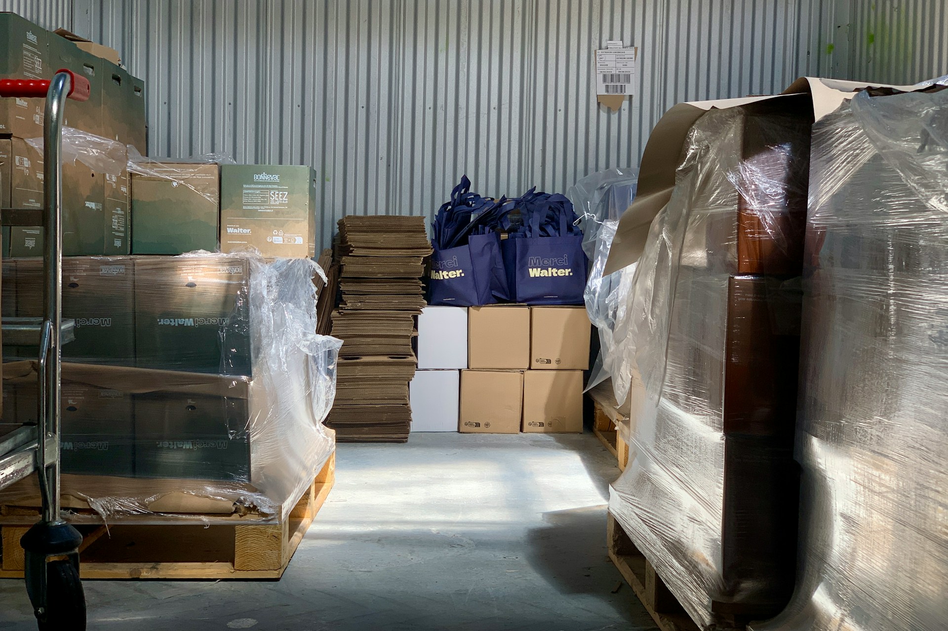 Boxes, bags, and stacked cardboard in a storage room with metal walls.